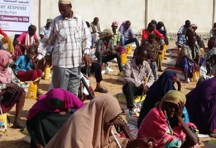 Families seated with rice sacks and cooking oil under a Somalia Drought Response banner in Banadir, 2017