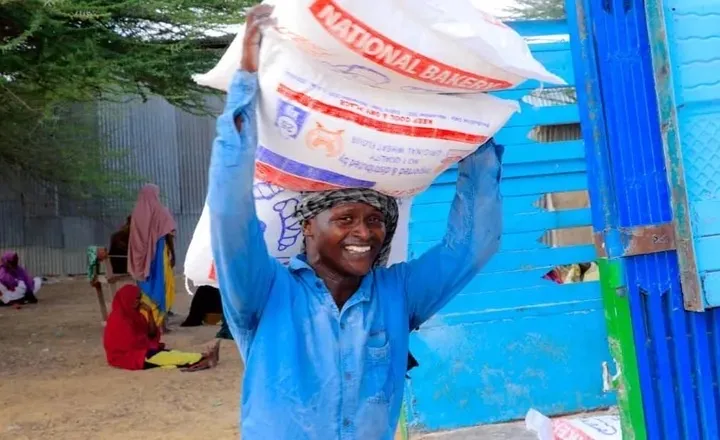 A smiling man carries a sack of National Bakery flour on his shoulder outside a blue-painted building
