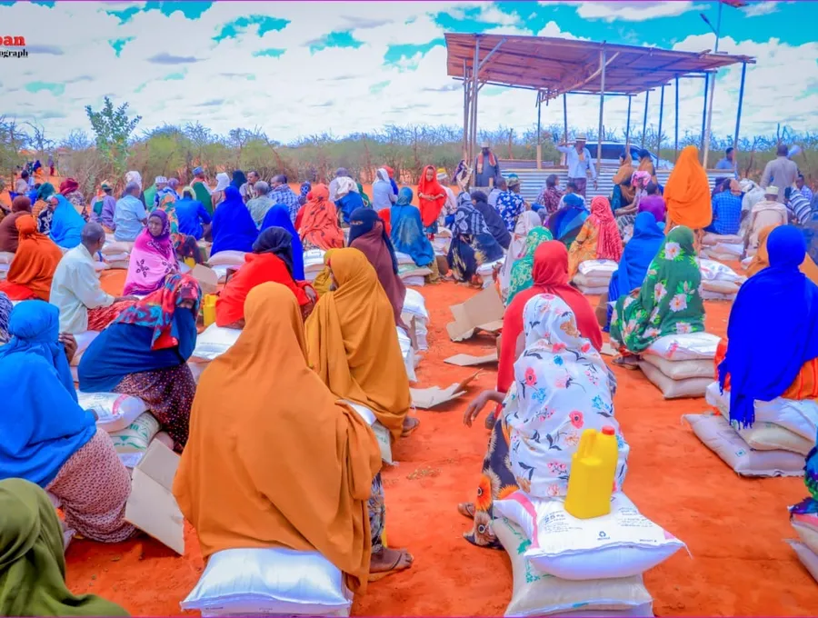 Families seated with sacks of food staples at a HARO distribution under an open sky