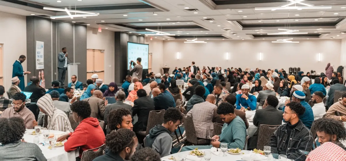 Guests seated at round tables during a HARO community event while a speaker addresses the room