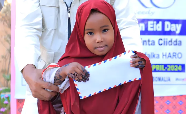 A girl in a red hijab holds her Eid gift envelope at a HARO Make Orphans Happy on Eid Day event, April 2024